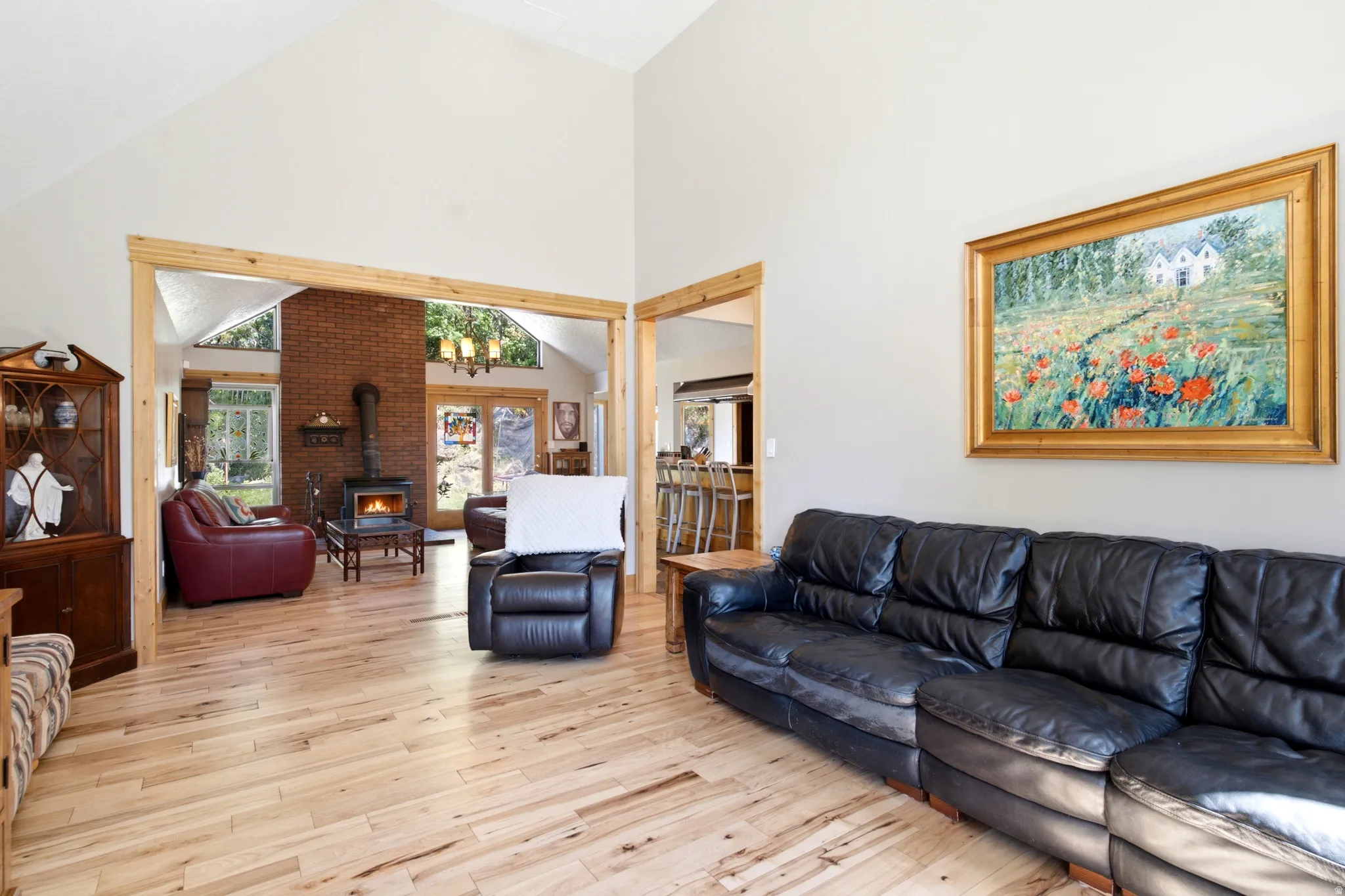 Vaulted ceiling, light wood-finish flooring, exposed wood trim, brick accent wall, and a built-in wood-burning stove
