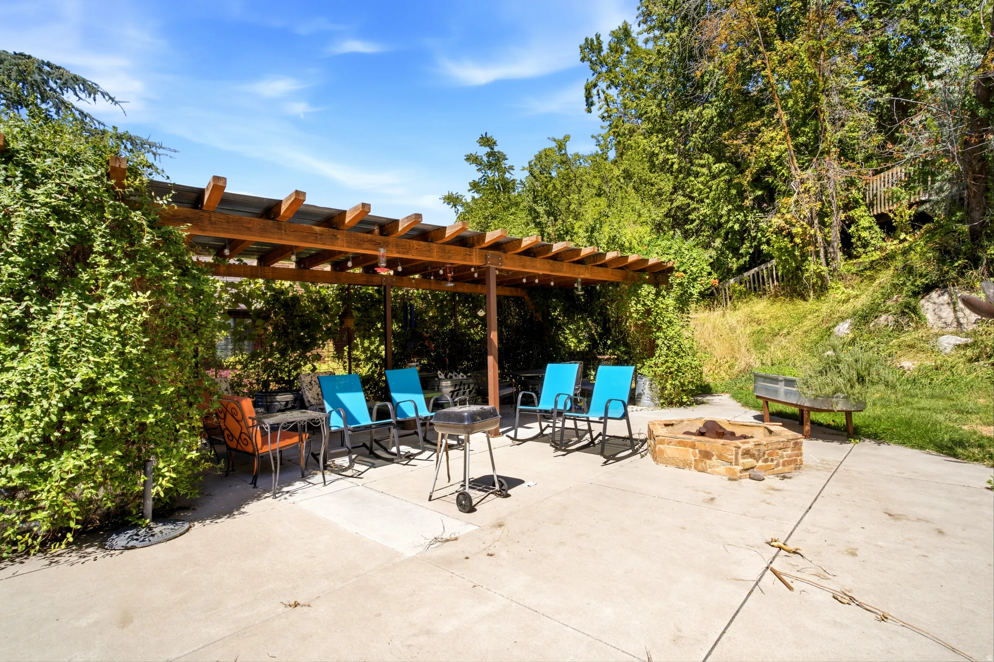 Expansive concrete patio featuring a wood pergola, string lighting, and a stone fire pit