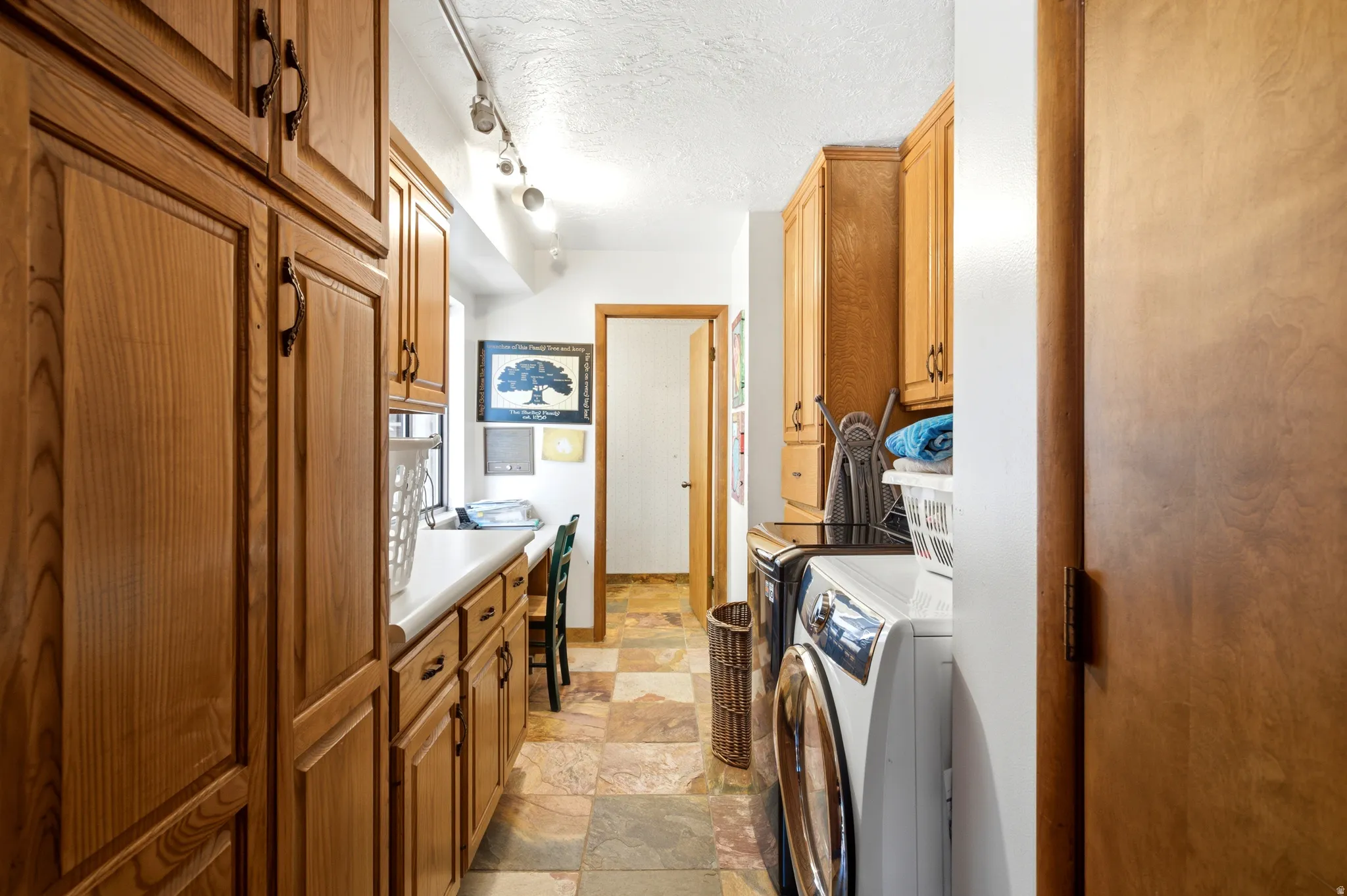 Extensive wood cabinetry, white countertops, tile flooring, track lighting, and a built-in workspace