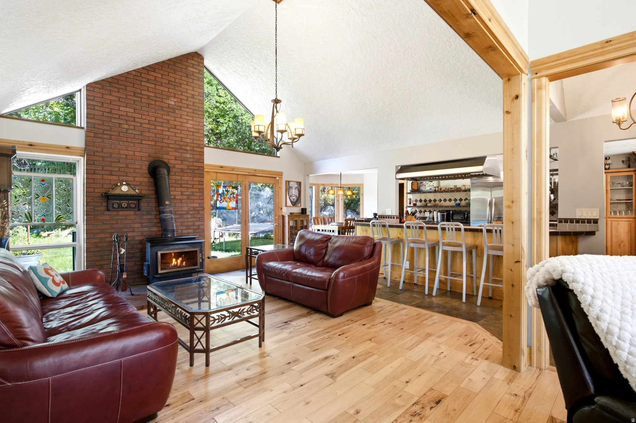Vaulted ceiling with exposed wood beams, brick fireplace with wood-burning stove, wood-finish flooring, French doors, and a built-in bar