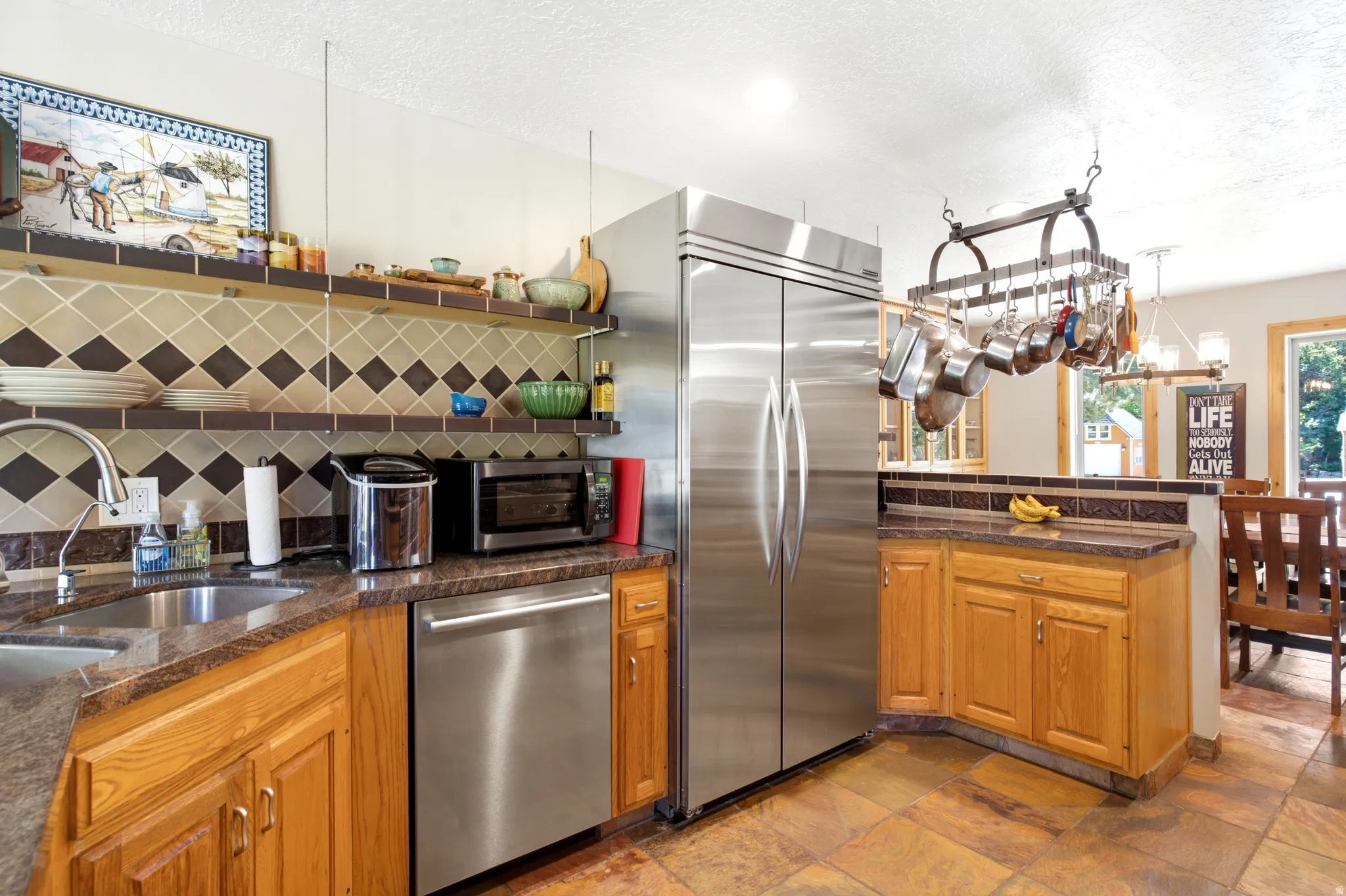 Stainless steel appliances, wood cabinetry, stone countertops, tiled backsplash, and pot rack