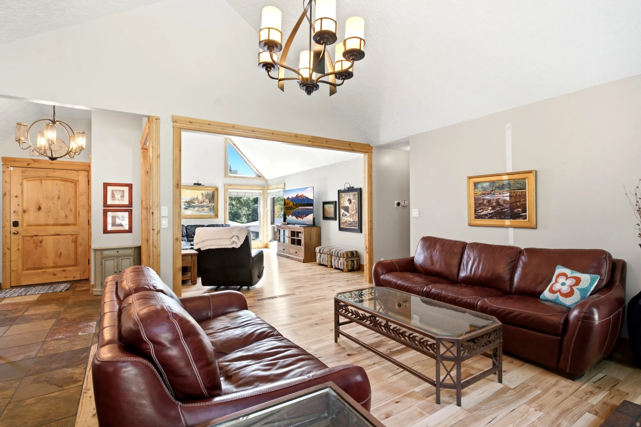 Vaulted ceiling with an ornate chandelier, wood-finish flooring, and a natural wood-trimmed doorway