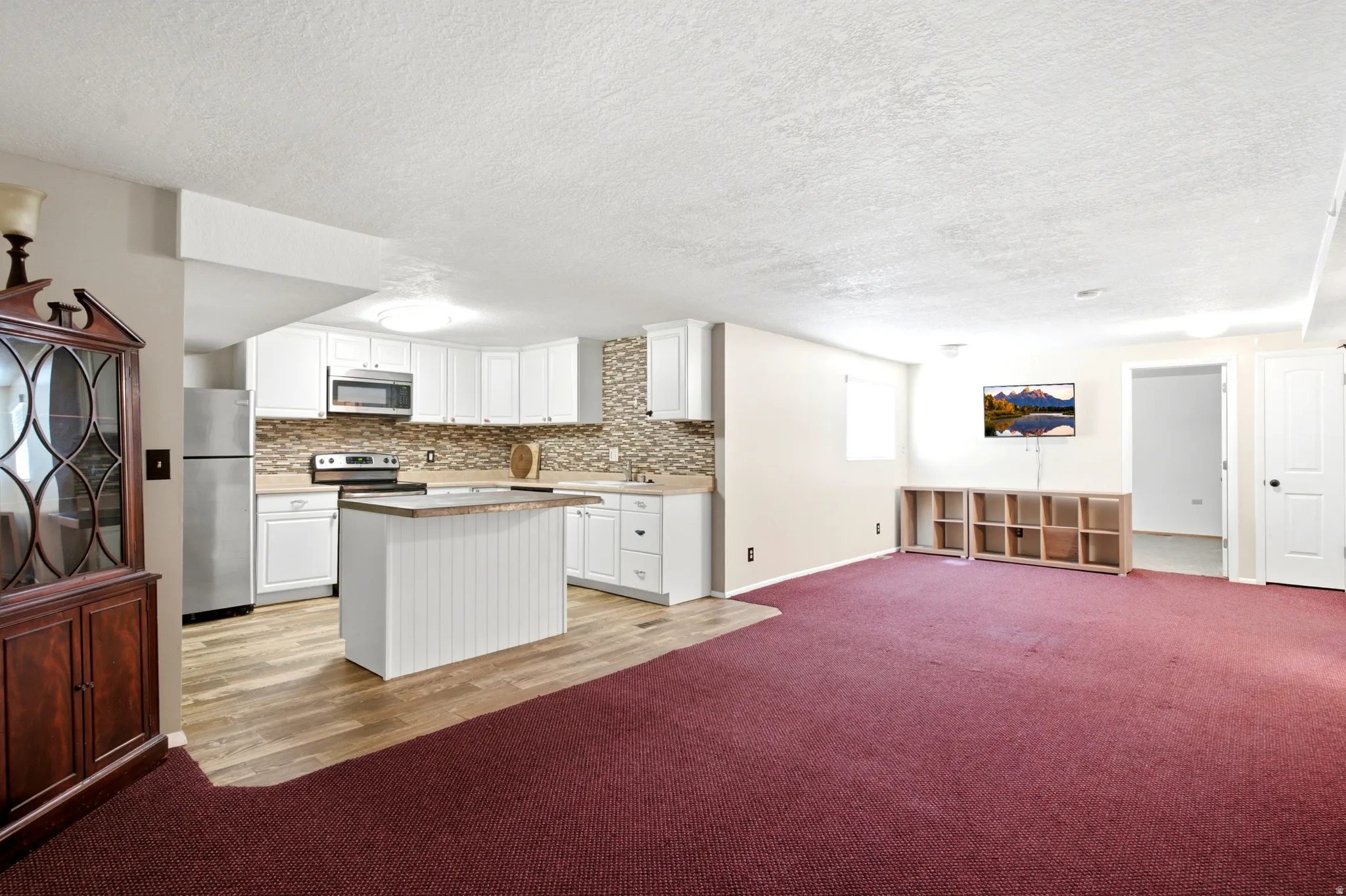 White cabinetry with stainless steel appliances, a center island, and wood-finish flooring