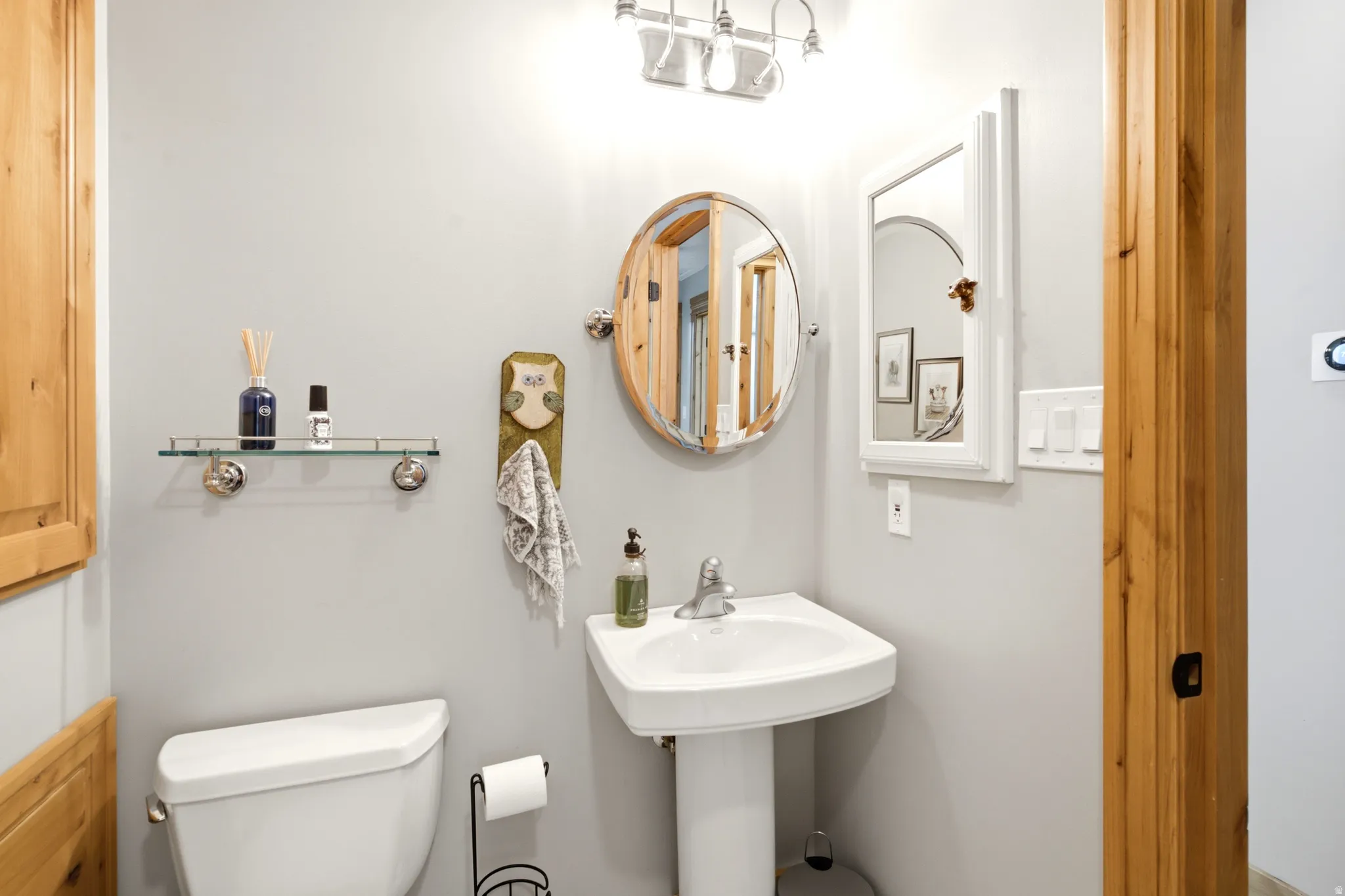Pedestal sink, wall-mounted oval mirror, wall-mounted glass shelf, white wall-mounted medicine cabinet, and wood-finish door frames