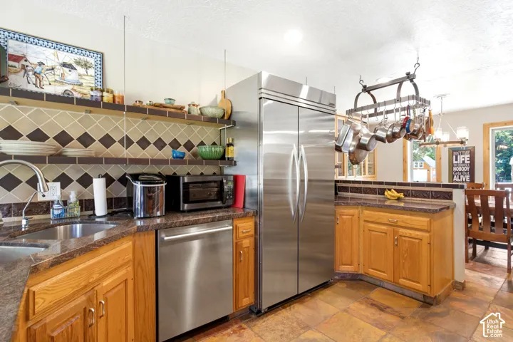Stainless steel appliances, wood cabinetry, stone countertops, tiled backsplash, and pot rack