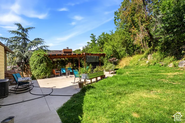 Expansive concrete patio with a wooden pergola, adjacent to a sloped grassy area