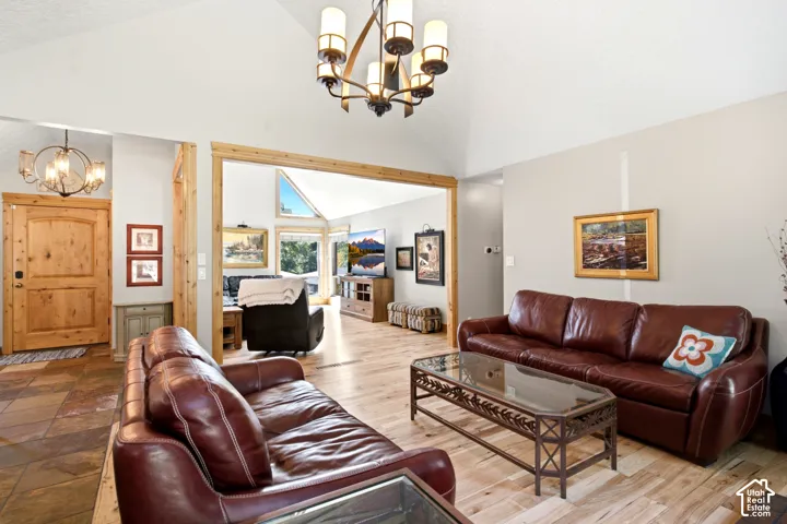 Vaulted ceiling with an ornate chandelier, wood-finish flooring, and a natural wood-trimmed doorway