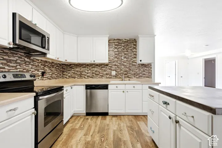 Kitchen with white cabinetry, stainless steel appliances, wood-finish flooring, and a mosaic tile backsplash