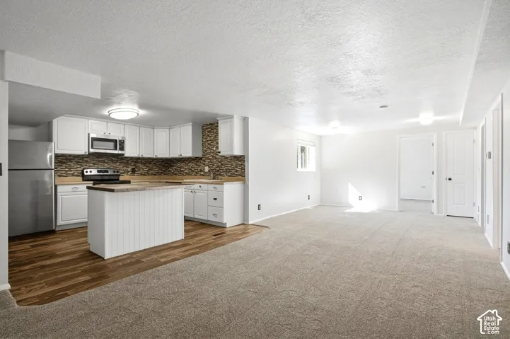 Open-concept living area featuring a kitchen with white cabinetry, stainless steel appliances, a center island with beadboard paneling, and wood-finish flooring
