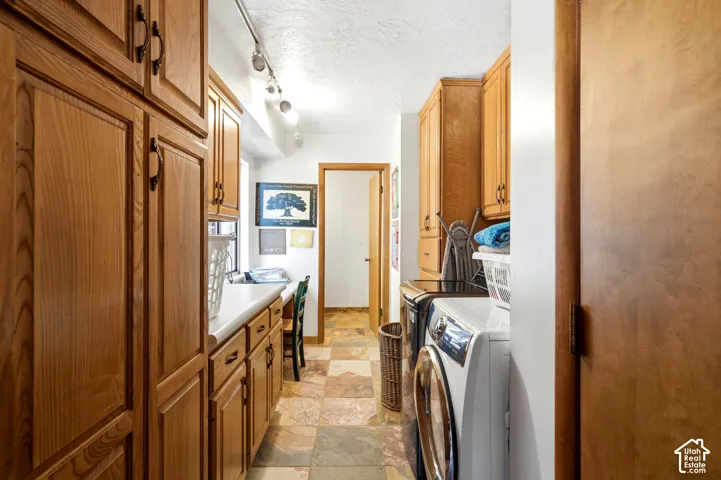 Extensive wood cabinetry, white countertops, tile flooring, track lighting, and a built-in workspace