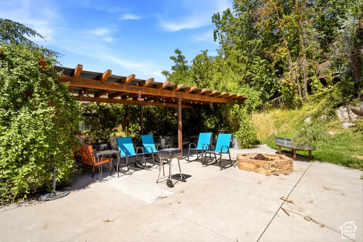 Expansive concrete patio featuring a wood pergola, string lighting, and a stone fire pit