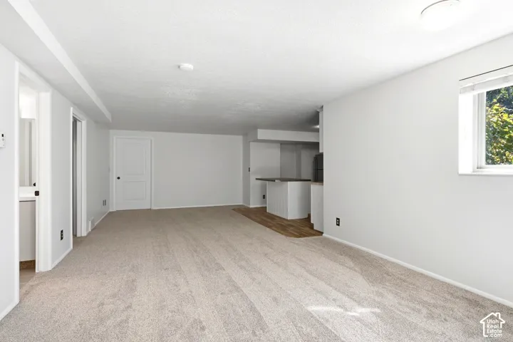 Expansive room with neutral carpeting, recessed lighting, and a distinct area featuring wood-finish flooring and a built-in counter