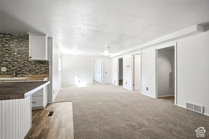 Open-concept living area featuring a kitchen island with beadboard paneling, white cabinetry, a mosaic tile backsplash, and wood-finish flooring