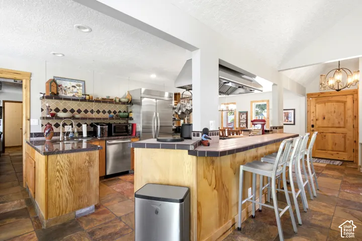 Kitchen featuring wood cabinetry, stainless steel appliances, a bar-height counter, a tiled backsplash, and recessed lighting