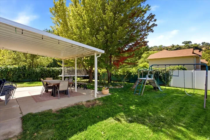 Fully fenced backyard yard designed to entertain: covered back patio & fire pit plus shade and fruit trees (pear, apple, peach) and a storage shed.