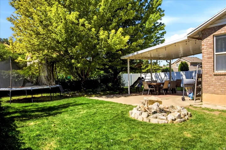 Fully fenced backyard yard designed to entertain: covered back patio & fire pit plus shade and fruit trees (pear, apple, peach) and a storage shed.