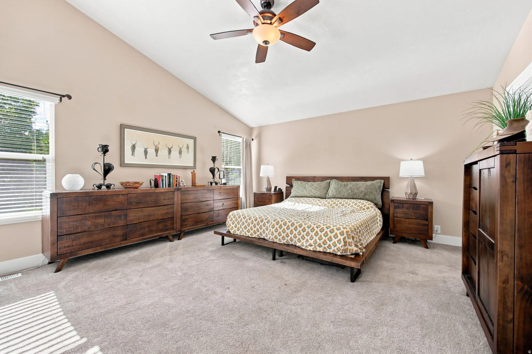 Vaulted ceiling with a ceiling fan, light-toned wall paint, two windows with blinds, and light-colored carpeting
