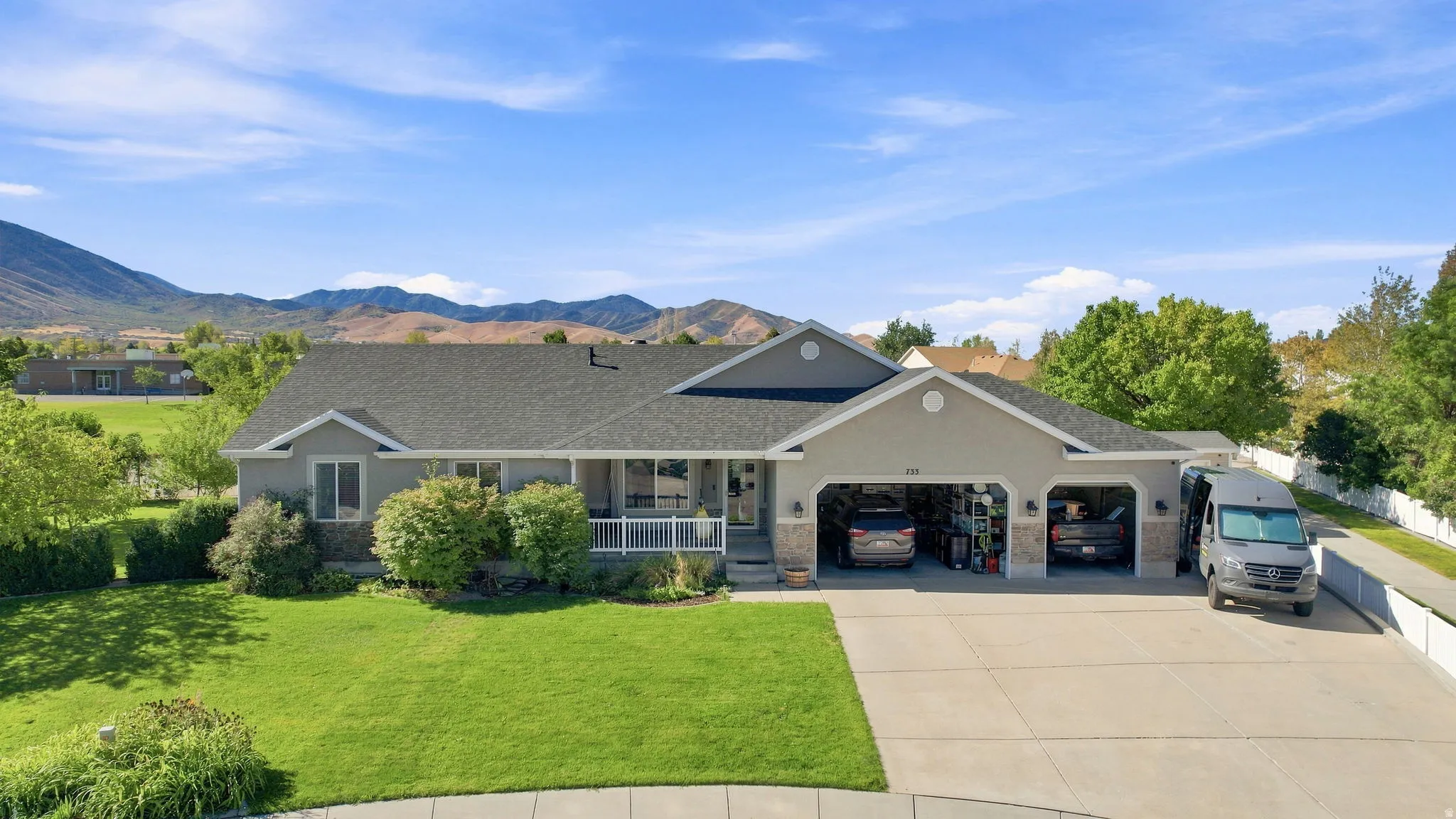 Ranch-style residence featuring a prominent two-car garage, expansive driveway, and a covered front porch with white railings