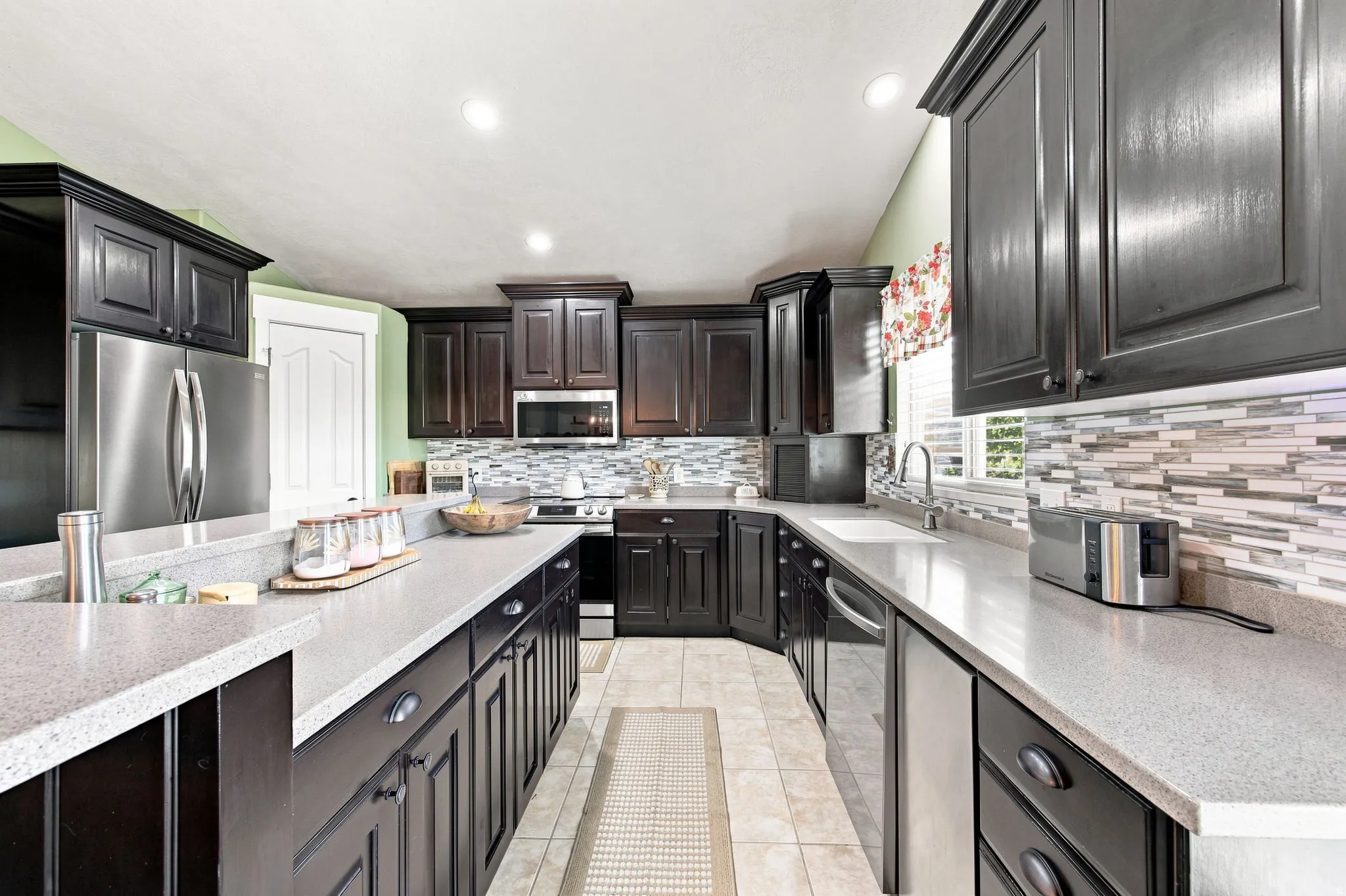 Kitchen featuring dark wood cabinetry, light-toned countertops, tile flooring, and a patterned tile backsplash