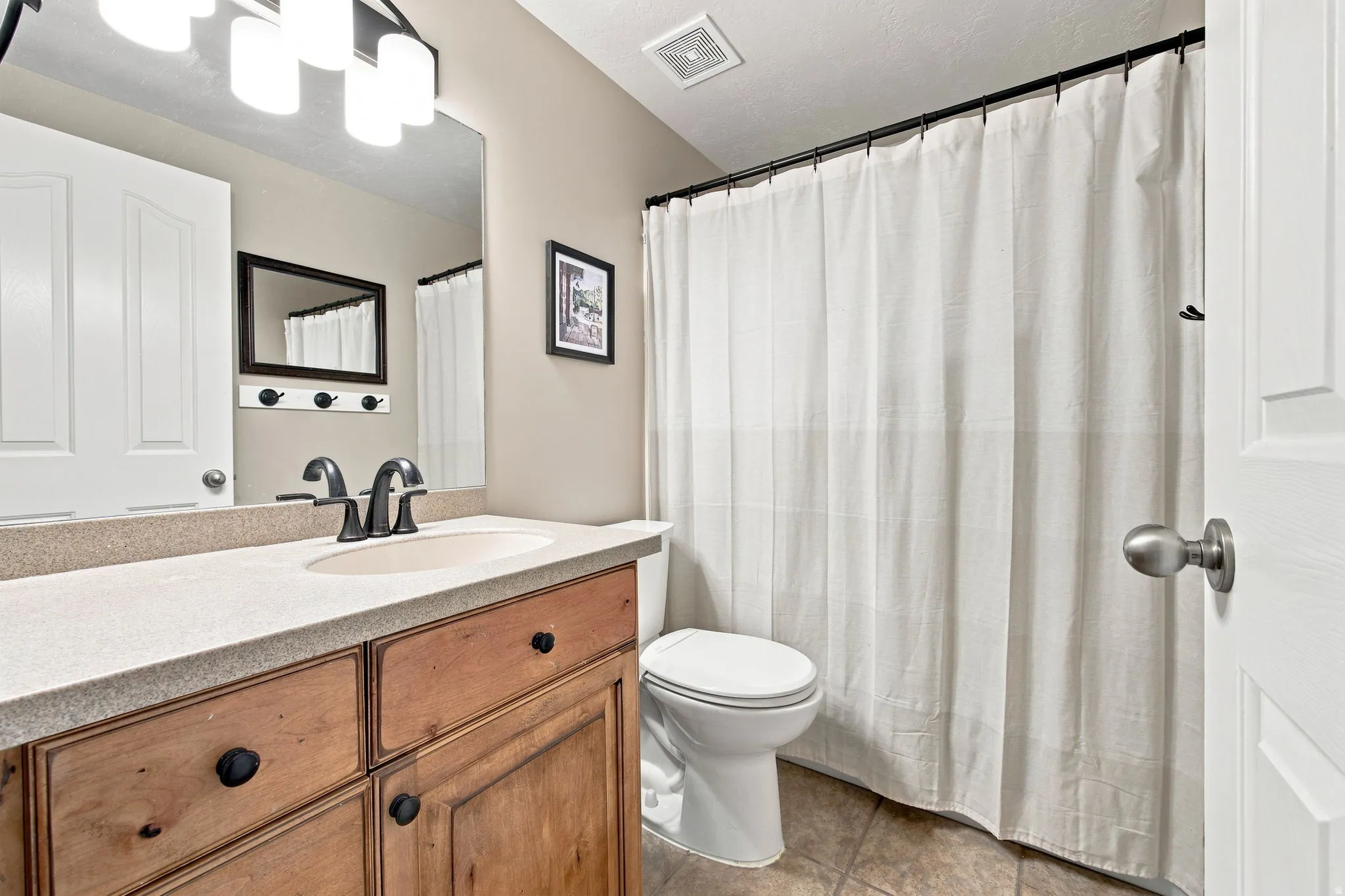 Wood-finish vanity with black hardware, integrated sink, and light-toned countertop
