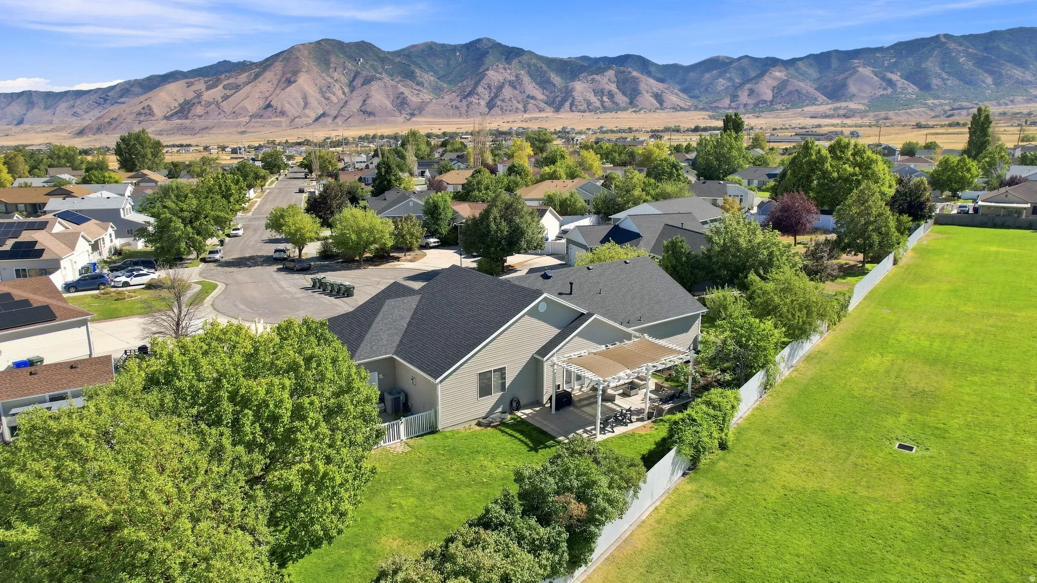Spacious yard with a white perimeter fence, a paved patio with a pergola, and mature trees