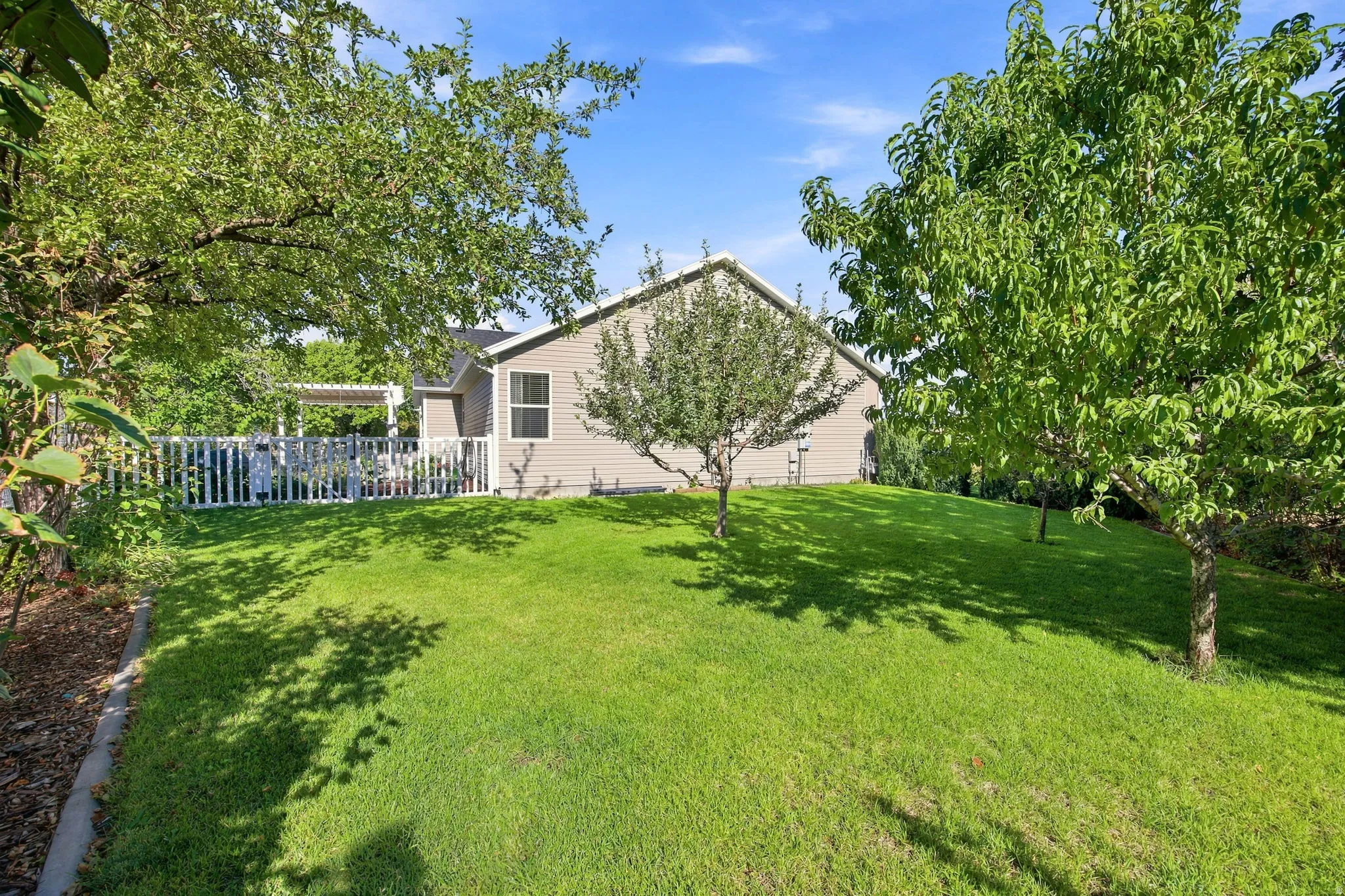 Expansive lawn with mature trees, a white picket fence, and a pergola-covered patio