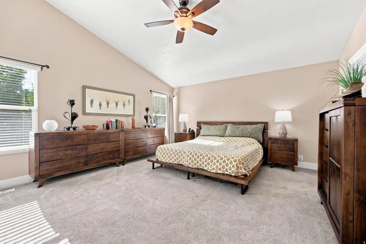 Vaulted ceiling with a ceiling fan, light-toned wall paint, two windows with blinds, and light-colored carpeting