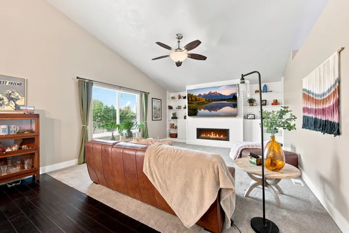 Vaulted ceiling, ceiling fan, built-in shelving, linear fireplace, and large window