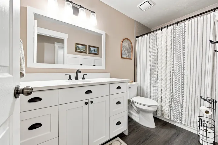 White vanity with ample storage, white countertop, dark wood-finish flooring, and a modern light fixture