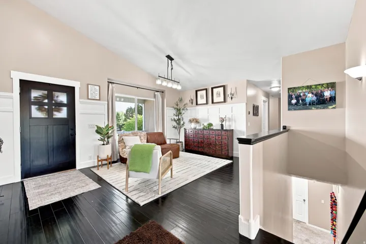 Vaulted ceiling, dark wood-finish flooring, wainscoting detail, black paneled entry door with frosted glass, and a modern linear chandelier