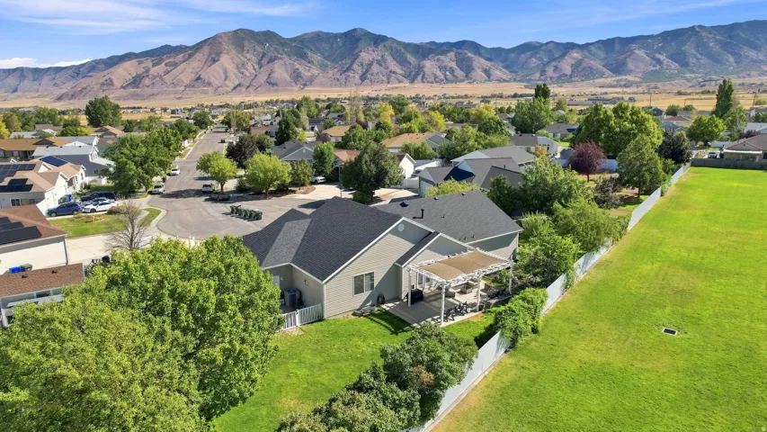 Spacious yard with a white perimeter fence, a paved patio with a pergola, and mature trees