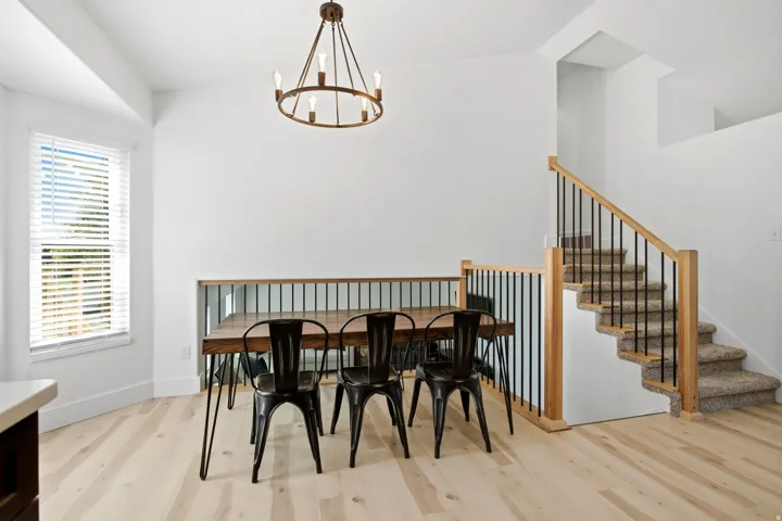 Vaulted ceilings, wood-finish flooring, staircase with natural wood newel posts and balusters, wrought iron chandelier, and white window blinds