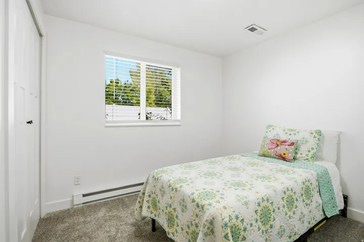 White walls, carpet flooring, and a single window with horizontal blinds