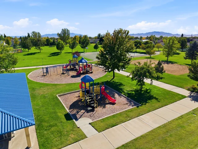 Expansive green space featuring two distinct playground structures, a covered picnic area, and paved walking paths