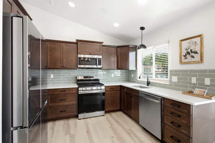 Kitchen featuring wood-finish cabinetry, stainless steel appliances, a subway tile backsplash, light countertops, and wood-finish flooring