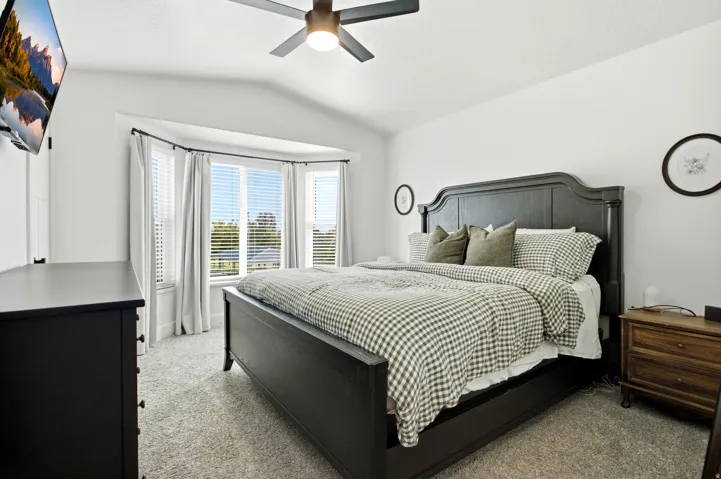 Bay window with white blinds, vaulted ceiling, ceiling fan with integrated lighting, and carpeted flooring