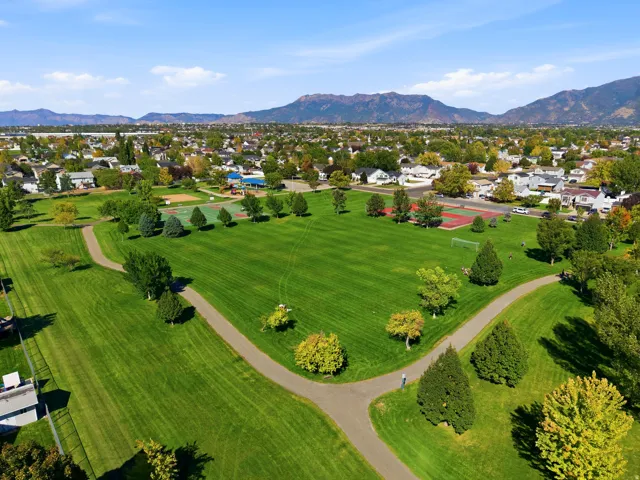Expansive parkland featuring a manicured lawn, paved walking paths, a sports court, and mature trees