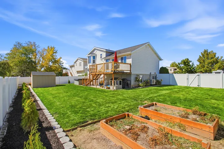 Expansive backyard featuring a manicured lawn, a raised wooden deck, a storage shed, and white vinyl perimeter fencing