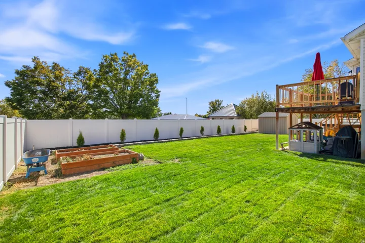 Expansive backyard with a manicured lawn, white privacy fencing, and raised garden beds