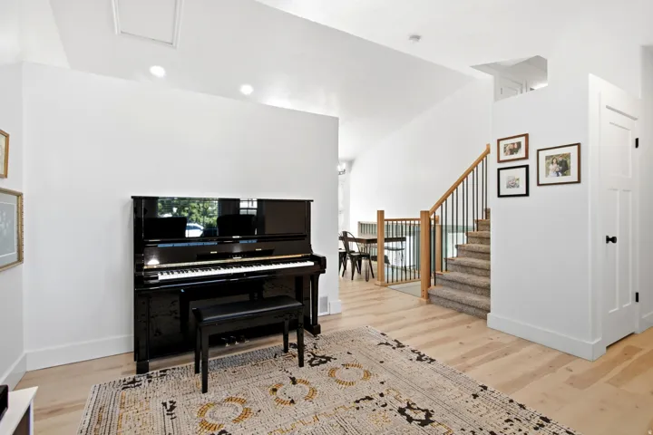 Light wood-finish flooring throughout, recessed ceiling lighting, staircase with natural wood handrail and black metal balusters, white paneled door with black hardware, and crisp white walls
