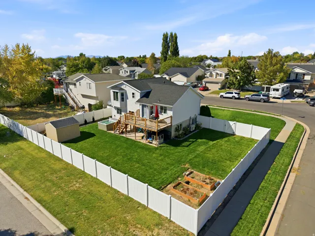 Expansive fenced backyard featuring a manicured lawn, multi-level wood deck, hot tub, garden beds, and storage shed