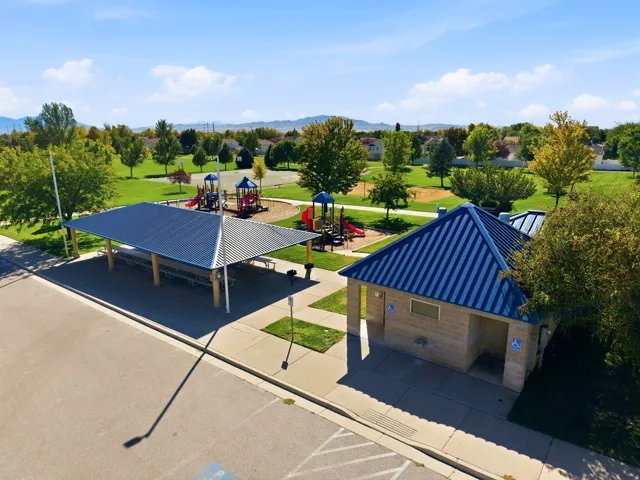 Expansive green space featuring playground equipment, a covered picnic area with tables, and a restroom facility with a blue metal roof