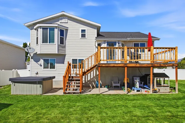 Expansive backyard featuring a manicured lawn, a raised wooden deck with railings, and a lower-level concrete patio