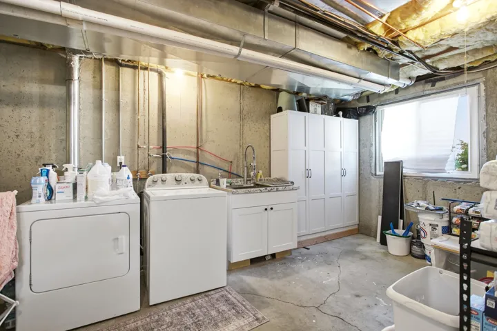 Laundry area featuring a utility sink, white cabinetry, a window, and exposed overhead utilities