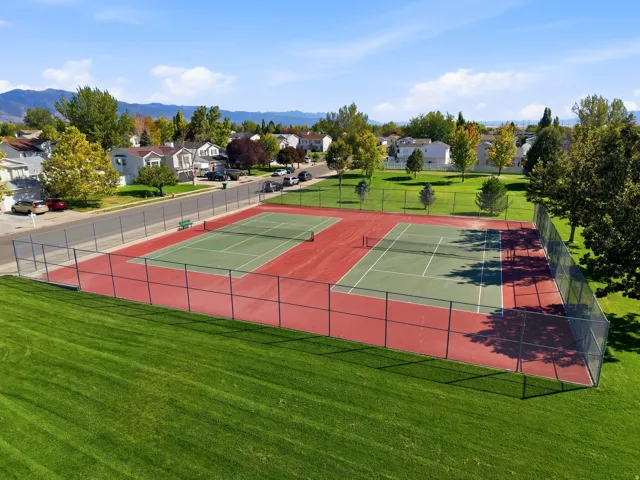 Expansive green space featuring two tennis courts with green playing surfaces and red surrounds, enclosed by chain-link fencing