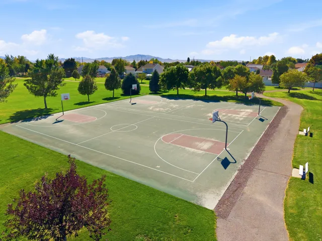 Outdoor basketball court with multiple hoops, surrounded by green lawns and mature trees