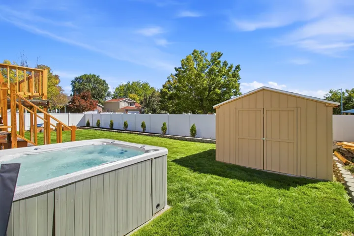 Spacious yard featuring a swim spa, a wooden playset, a utility shed, and a white privacy fence