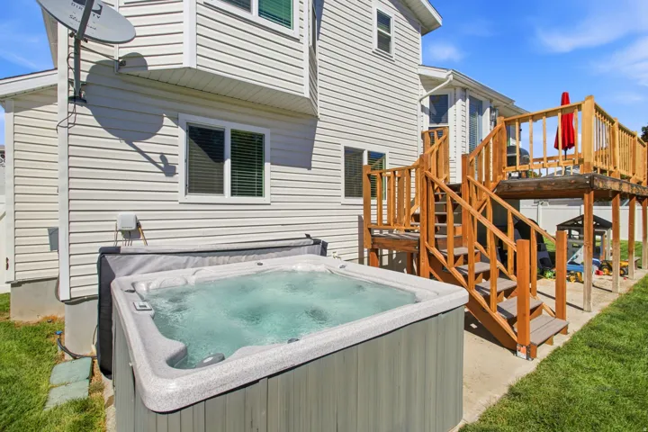 Outdoor spa, multi-level wood deck, white vinyl siding, privacy fencing, and green lawn