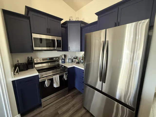 Stainless steel appliances, wood-finish flooring, white countertops, and dark blue cabinetry