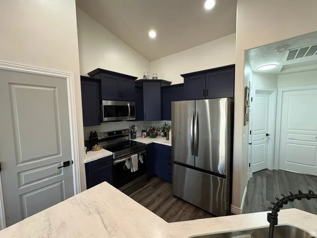 Kitchen featuring dark blue cabinetry, stainless steel appliances, light-toned countertops, vaulted ceiling, and wood-finish flooring